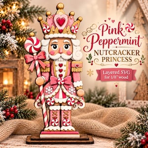 Peut inclure: Une figurine de casse-noisette princesse décorative dans des tons rose, blanc et or, tenant un bâton en forme de sucette à la menthe. Le texte indique Pink Peppermint NUTCRACKER PRINCESS Layered SVG for 1/8" wood. Orné de cœurs et flocons.