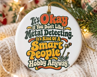 May include: A round white ceramic ornament featuring the text It's Okay If You Don't Like Metal Detecting. It's Kind Of A Smart People Hobby Anyway. The design includes a small illustration of a metal detector and a gold hanging string.