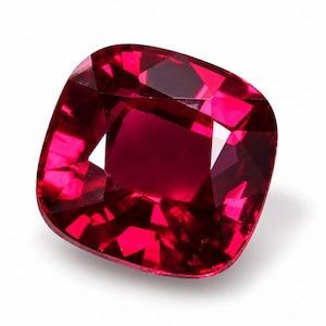 May include: A cushion-cut ruby gemstone with a deep, vibrant red colour and multiple facets that create a reflective, sparkling appearance. The stone has a square shape with rounded corners and exhibits high clarity and light refraction.