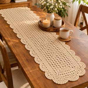 Peut inclure: Un long chemin de table en crochet de couleur crème, de forme rectangulaire, doté d'un bord festonné et d'un motif ajouré complexe. Le chemin de table est posé à plat, présentant un design géométrique répétitif et une bordure décorative.