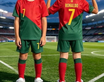May include: A soccer uniform set featuring a red and green color-blocked jersey and shorts. The jersey displays the number 7 on the front and the name RONALDO with the number 7 on the back. The set includes red soccer socks and white sneakers.
