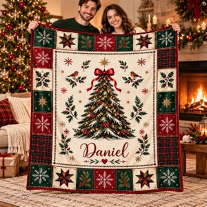 Könnte beinhalten: Eine rechteckige Wohndecke mit einem zentralen Weihnachtsbaum mit roter Schleife, zwei Vögeln und dem in Schreibschrift gedruckten Namen Daniel. Der Rand besteht aus abwechselnd grünen und roten Quadraten mit Schneeflocken, Sternen und Stechpalmen.