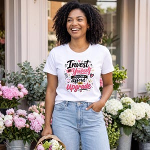 Peut inclure: Un t-shirt blanc à manches courtes avec le texte noir et rose Invest in Yourself YOU CAN afford THE UPGRADE accompagné de petits graphismes en forme de cœur, d'étoile et de couronne. Le t-shirt est porté avec un jean bleu clair.