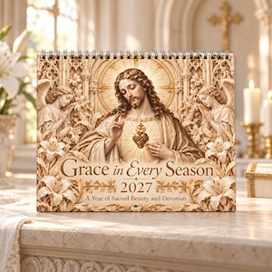 May include: A 2027 wall calendar titled Grace in Every Season: A Year of Sacred Beauty and Devotion. The cover features a central illustration of Jesus with a Sacred Heart, flanked by two angels and lilies in a beige, ornate architectural setting.