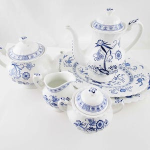 May include: A white porcelain tea set with blue floral designs. The set includes a teapot, a coffee pot, a creamer, a sugar bowl, and plates. The tea set is a classic design, perfect for serving tea or coffee.