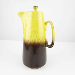May include: A yellow and brown ceramic coffee pot with a lid. The pot has a flared spout and a handle.