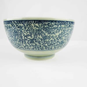 May include: A white ceramic bowl with a blue and white pattern. The pattern is a repeating design of stylized leaves and swirls.