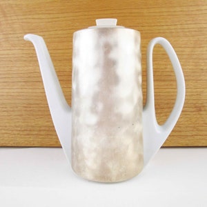 May include: White ceramic coffee pot with a silver-grey glaze and a unique spout design.