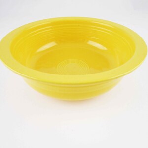 May include: A bright yellow ceramic bowl with a wide rim and a slightly rounded bottom. The bowl has a smooth, glossy finish.