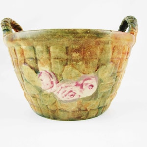May include: A green and brown ceramic planter with a woven rim and floral design. The planter features pink and white flowers and leaves.