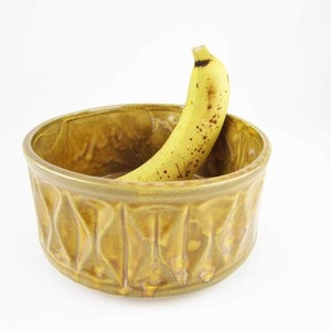 May include: A yellow ceramic bowl with a textured, leaf-like design. A yellow banana is resting inside the bowl.