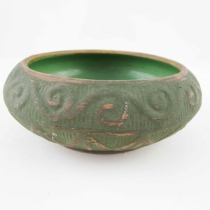 May include: A green ceramic bowl with a textured exterior and a smooth, green interior. The bowl has a rounded shape with a brown rim and decorative swirl patterns around the exterior. The bowl is approximately 6 inches in diameter.