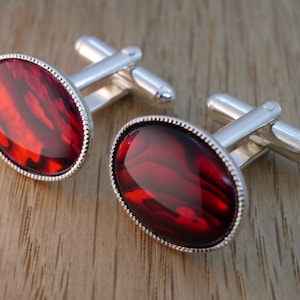 May include: A pair of silver cufflinks with red oval-shaped stones set in a silver bezel.