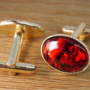 Peut inclure: Une paire de boutons de manchette en or avec des pierres de verre rouge marbrées. Les boutons de manchette ont un design simple et classique.