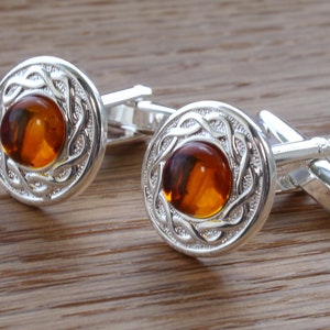 May include: A pair of silver cufflinks featuring a Celtic knot design and amber gemstones in the centre.