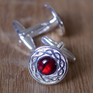 May include: A pair of silver cufflinks with a red gemstone set in a Celtic knot design.