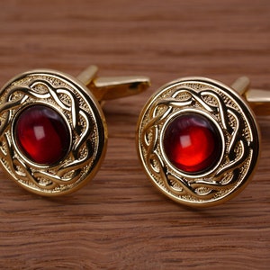 May include: A pair of gold cufflinks with red gemstone accents. The cufflinks feature a Celtic knot design.