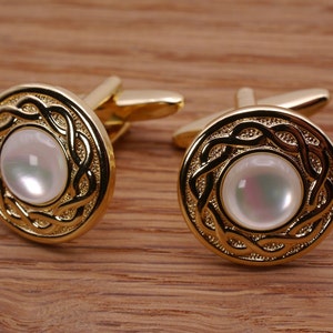 May include: A pair of gold cufflinks with a white mother-of-pearl inlay. The cufflinks feature a Celtic knot design.