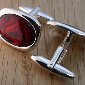 May include: A pair of silver cufflinks with a red oval-shaped stone in the center.