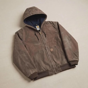 May include: A brown hooded jacket featuring a full-length front zip, a dark blue interior lining, and ribbed cuffs and hem. The garment includes a front pouch pocket with a small rectangular brand label attached to the upper right corner.