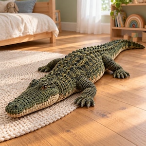 Peut inclure: Un grand crocodile en crochet fait main, doté d'un corps texturé vert foncé et olive avec un ventre plus clair de couleur crème. Ce reptile en peluche présente des écailles détaillées, quatre pattes robustes avec des griffes et des yeux ambrés.