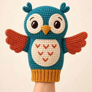 May include: A teal crochet owl hand puppet featuring large white circular eyes with dark brown pupils, a yellow triangular beak, and orange wings. The belly is white with orange V-shaped embroidery, and the base is a ribbed mustard yellow cuff.