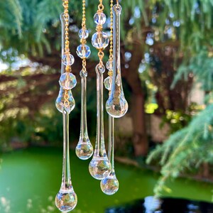 K&ouml;nnte beinhalten: Ein Kristall-Sonnenf&auml;nger mit mehreren tropfenf&ouml;rmigen Glasprismen, die an goldenen Ketten h&auml;ngen. Die Prismen sind klar und reflektieren das Licht.