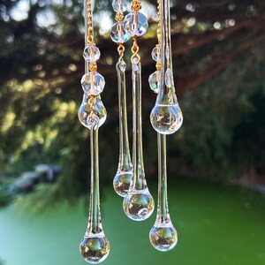 K&ouml;nnte beinhalten: Ein Kristall-Sonnenf&auml;nger mit f&uuml;nf tropfenf&ouml;rmigen Prismen, die an einer goldenen Kette h&auml;ngen. Die Prismen sind klar und reflektieren das Licht.