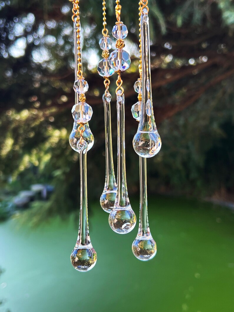 K&ouml;nnte beinhalten: Ein Kristall-Sonnenf&auml;nger mit f&uuml;nf tropfenf&ouml;rmigen Prismen, die an einer goldenen Kette h&auml;ngen. Die Prismen sind klar und reflektieren das Licht.
