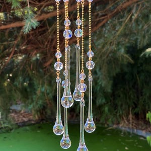 K&ouml;nnte beinhalten: Ein Kristall-Tropfen-Windspiel mit sechs tropfenf&ouml;rmigen Kristallen, die an goldenen Ketten h&auml;ngen. Die Kristalle sind klar und schimmernd, und die Ketten sind mit kleinen, klaren Perlen verziert.