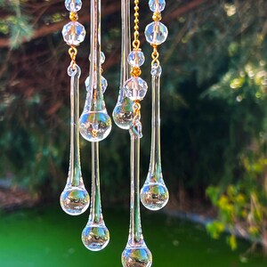 K&ouml;nnte beinhalten: Ein Kristall-Sonnenf&auml;nger mit mehreren tropfenf&ouml;rmigen Prismen, die an einer goldenen Kette h&auml;ngen. Die Prismen sind klar und reflektieren das Licht.