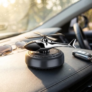 May include: A shiny chrome-coloured helicopter ornament mounted on a circular black base with a solar panel top. The helicopter features a black cockpit section and a rotating propeller assembly, designed as a decorative car dashboard accessory.