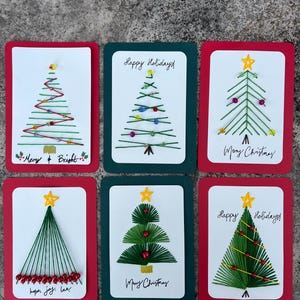May include: Six rectangular greeting cards featuring embroidered Christmas tree designs. Each card displays unique thread-stitched trees decorated with beads, stars, and handwritten text including Merry & Bright, Happy Holidays, and Merry Christmas.