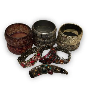 May include: A collection of assorted bracelets and a hair clip. The set includes two thick bangles with brown patterns, two metallic grey bangles, a gold-toned filigree bangle, three ornate bracelets with red and orange rhinestones, and a hair clip.