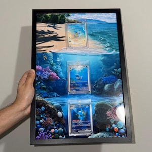 May include: A rectangular black frame containing three trading cards displayed vertically against a printed background of a beach and underwater coral reef scene. The cards feature Squirtle, Wartortle, and Blastoise in clear protective cases.
