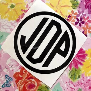 Peut inclure: Un autocollant de monogramme noir et blanc avec les lettres "JUP" dans un cercle. L'autocollant est sur un fond blanc.