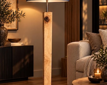 Peut inclure: Un lampadaire composé d'un long poteau en bois clair de forme rectangulaire avec un nœud apparent, fixé sur une base carrée noire. La lampe est surmontée d'un grand abat-jour cylindrique en tissu bleu marine et d'un col en métal chromé.
