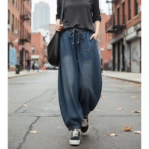 Op de afbeelding: Losvallende blauwe denim joggingbroek met een elastische tailleband met trekkoord, een enkele opgestikte zak op de linkerdij en elastische boorden bij de enkels. De broek heeft een vervaagde wassing en een ruimvallend model.