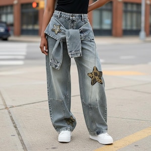 May include: High-waisted, wide-leg denim jeans in a faded blue wash. The jeans feature a denim jacket tied around the waist, creating a layered effect. Three star-shaped patches with a brown and black leopard print are visible on the legs.