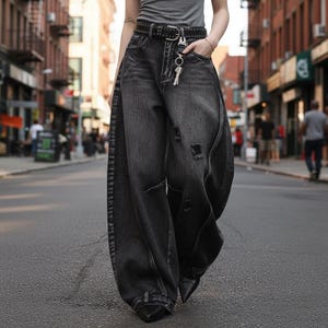 Op de afbeelding: High-waisted jeans met wijde pijpen in een gewassen zwarte denim afwerking. De jeans heeft een versleten look met kleine scheurtjes, een zwarte riem met studs en een zilverkleurige metalen clip aan de riemlus met een sleutelbos.