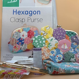 Puede incluir: Un kit de manualidades para un monedero hexagonal con cierre, que incluye un folleto de patrones, un marco de metal, un carrete de hilo gris, clips de plástico y un monedero terminado hecho de hexágonos de tela estampada.