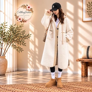 May include: A long, cream-colored sherpa fleece coat with a hood, long sleeves, and a front button closure. The coat features tan trim along the edges, two front pockets with zippers, and long drawstrings. A black baseball cap with an R is worn.