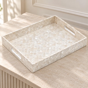 May include: A rectangular serving tray featuring a surface covered in iridescent, off-white shell pieces arranged in a repeating scalloped pattern. The tray has raised sides and two integrated cutout handles on the shorter ends.