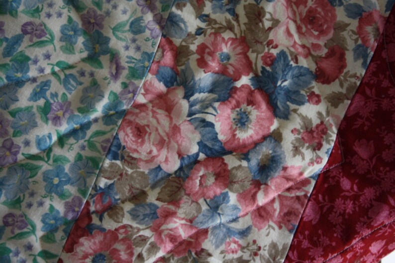 May include: A patchwork quilt featuring a variety of floral patterns in shades of pink, blue, and white. The quilt is made from different fabrics and textures, creating a unique and interesting design.