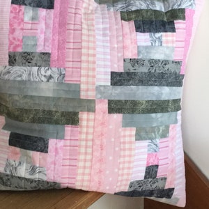 May include: A pink and gray patchwork pillow with a variety of patterns, including floral, plaid, and striped designs.