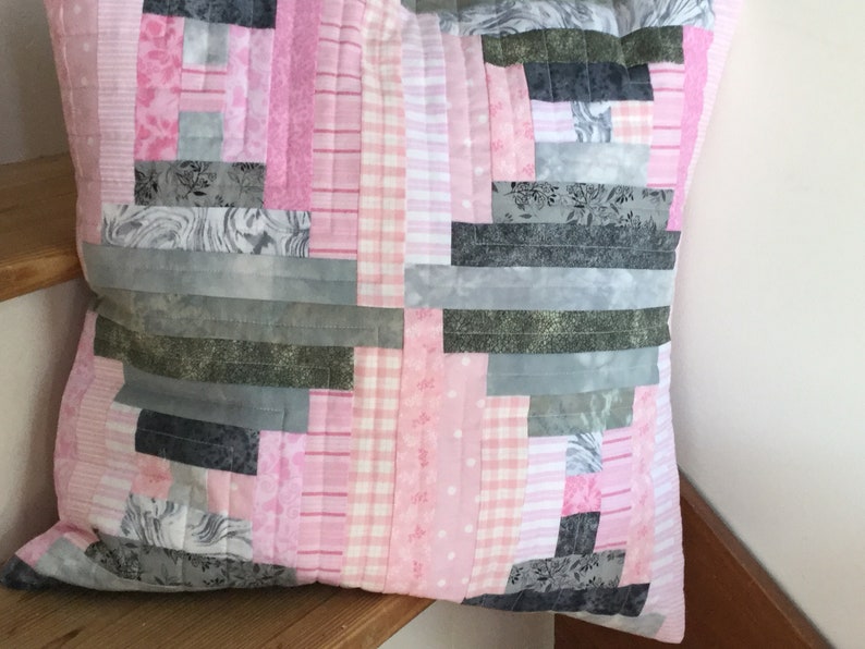 May include: A pink and gray patchwork pillow with a variety of patterns, including floral, plaid, and striped designs.
