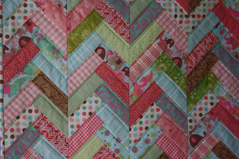 May include: A patchwork quilt with a chevron pattern in shades of pink, green, blue, and brown. The quilt is made of various fabrics with different patterns, including polka dots, stripes, and floral prints.