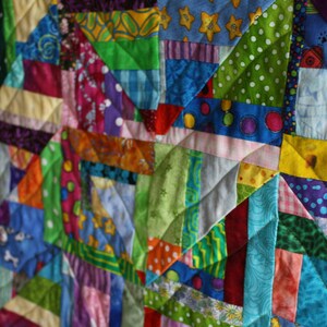 May include: A colourful patchwork quilt made from various fabrics in shades of blue, green, red, yellow, and purple. The quilt is made up of many different sized squares and triangles, creating a complex and interesting pattern.