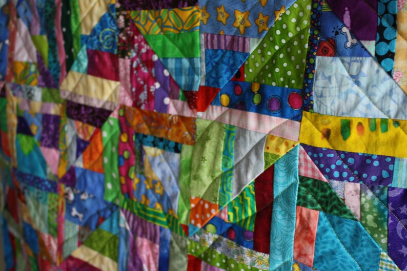 May include: A colourful patchwork quilt made from various fabrics in shades of blue, green, red, yellow, and purple. The quilt is made up of many different sized squares and triangles, creating a complex and interesting pattern.