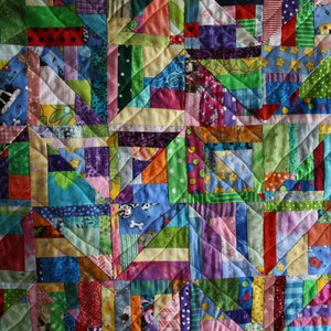 May include: A colourful patchwork quilt featuring a range of fabrics and patterns, including stripes, polka dots, and floral prints. The quilt is made up of squares and rectangles, and the seams are visible.